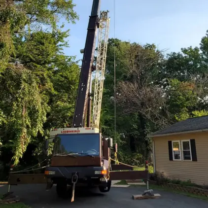 Crane truck with its boom raised, parked in a residential driveway in preparation for a tree removal.