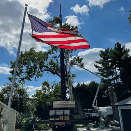 American flag waving on a pole with a bucket truck's aerial boom and trees visible in the background.