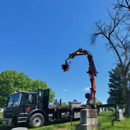 Truck-mounted knuckle-boom crane with a grapple saw attachment reaching into a bare tree over a residential street.