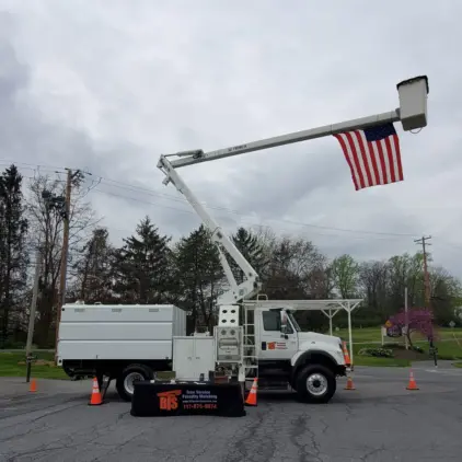 White chip truck fitted with a hydraulic boom crane, parked at a job site with traffic cones and a folding display table set out.