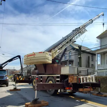 Large mobile crane with outriggers deployed on a residential street for a tree job, with a bucket truck parked nearby.