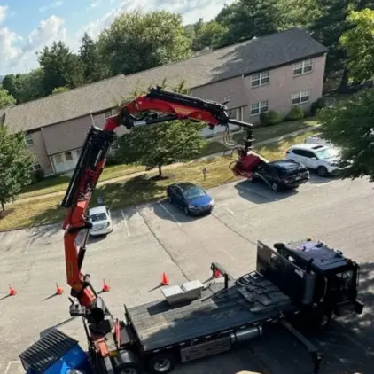 Aerial view of a knuckle-boom truck reaching its grapple arm across a parking lot to remove tree branches near townhomes.